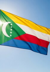 A vibrant flag of the Comoros, displaying its green, yellow, red, white, and blue colors against a clear blue sky.