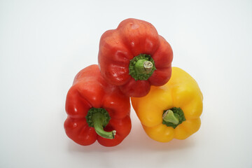 A vibrant and healthy arrangement of two red bell peppers and one yellow bell pepper, stacked artfully against a clean white background, highlighting their fresh appeal for culinary creations