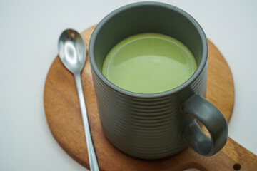 A warm cup of matcha green tea latte served in a contemporary grey ceramic mug on a wooden coaster, a perfect healthy morning ritual