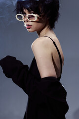 Stylish woman with short hair wearing sunglasses and a black top in a moody studio setting