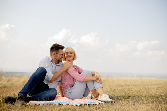Young couple enjoys a peaceful moment together on a blanket in a grassy field under a clear sky - Powered by Adobe