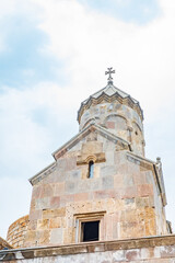 Close-up view of an ancient stone church tower topped with a cross, highlighting historic religious architecture against a soft blue sky. A beautiful symbol of faith and heritage of Tatev monastery