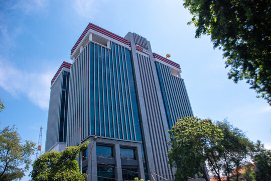 Surabaya, Indonesia - September 15, 2025: OJK Surabaya skyscraper photographed from low perspective with a vivid blue sky backdrop, emphasizing height and contemporary style.