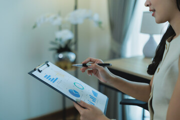 Woman holding a clipboard with data charts and graphs, pointing with a pen, reviewing financial performance and analyzing business report in a professional office setting
