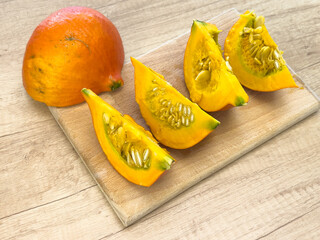 Fresh Hokkaido pumpkin cut into wedges on wooden board, showing seeds and vibrant orange flesh, ready for cooking or seed drying.

