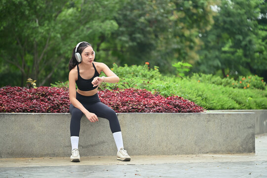 Young woman runner tracking wellness data in smartwatch in the park
