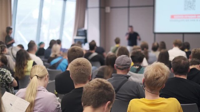 Attendees seated in modern conference room listen attentively to seminar speaker presenting topic.