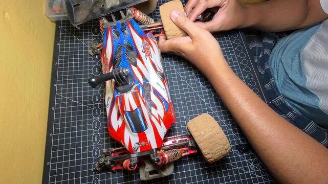 Footage of a mechanic removing a toy car tire. Videography of hand movements while unscrewing a locking bolt. RC toy car repair and maintenance. High Quality 4K 30 FPS