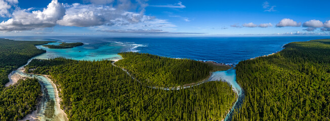 A stunning aerial panorama of Oro Bay on the Isle of Pines. The turquoise river of the natural pool winds through the pine forest to meet the rugged coastline of the Pacific Ocean © Anton Gots