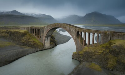 Ancient stone arch bridge spans a river valley, Iceland. Cloudy, mountainous landscape