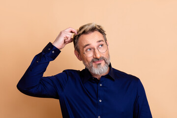 Portrait of a mature businessman in navy blue shirt scratching head with a puzzled expression against beige background
