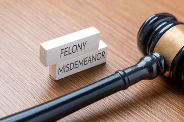 A judge’s gavel next to wooden blocks labeled Felony and Misdemeanor. Legal terms, criminal...