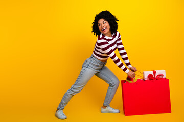 Excited woman pulling large red gift bag against a vibrant yellow backdrop for a shopping and holiday concept