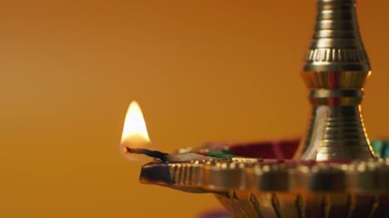 A close-up of a traditional oil lamp glowing warmly against a vibrant orange background during a festive celebration