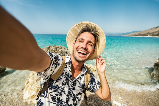 Handsome young man taking selfie picture with smart mobile phone outside - Happy tourist enjoying summer holiday at the beach - Traveling and technology life style concept	