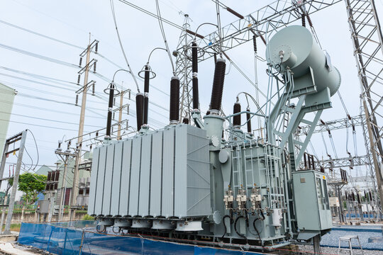 Large power transformer installed in high voltage substation. Features include cooling radiator, bushing insulators, control panel, and steel support. Key component for electric energy transmission.
