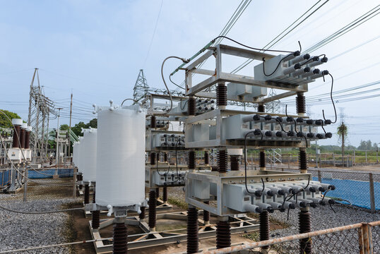 Close-up view of outdoor high voltage capacitor bank with cylindrical reactors and stacked capacitor units, used for reactive power compensation and voltage stability in substations.