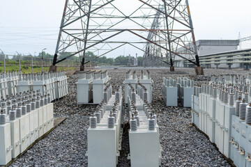 Capacitor banks aligned in rows under steel transmission tower at high voltage substation, electrical equipment designed for reactive power control, energy efficiency, and grid reliability.