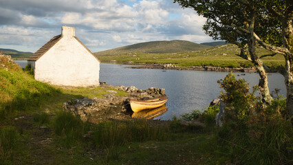 Naklejka premium Traditional stone cottage fisherman hut on the rocky lakeside of Connemara national park Ireland at sunrise, nature background