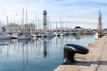 Barcelona, Spain-April 12, 2023. A tranquil scene of a sailboats gliding in the harbor with reflections on the still water, surrounded by Barcelona port vell and its nautical vessels