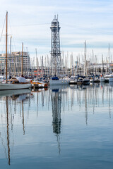 Barcelona, Spain-April 12, 2023. A tranquil scene of a sailboats gliding in the harbor with reflections on the still water, surrounded by Barcelona port vell and its nautical vessels