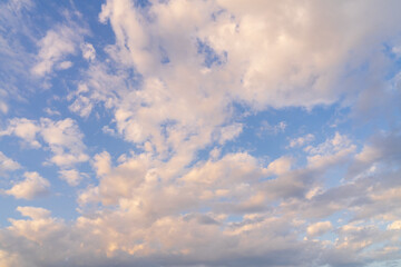 Beautiful background of a vast blue sky with fluffy white and pink clouds during a scenic golden hour sunset.