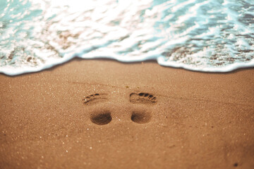 Footsteps on a clean sandy beach with ocean waves in the background