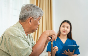 Obraz premium Senior Man with Cane Discussing Health with a Female Caregiver, Asian Elderly Man Holding Walking Stick During a Home Visit by a Nurse, Patient and a Medical Professional in a Consultation