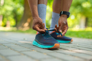 Close-up of athlete tying shoelaces before running in park. Man in sportswear preparing for outdoor...