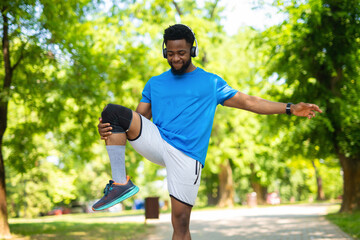 Young african american man stretching leg with knee support before outdoor run.
