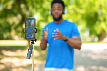 Smartphone on tripod filming african american man with headphones giving presentation outdoors.
