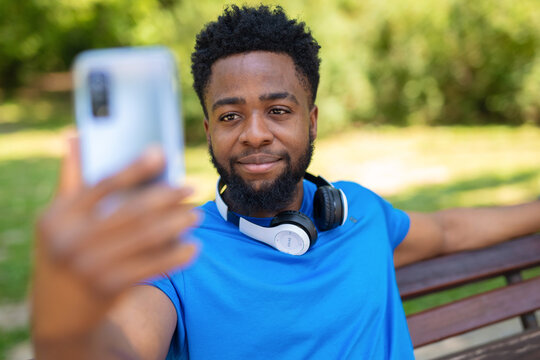 Young man with headphones taking a selfie on park bench using smartphone.
- Powered by Adobe
