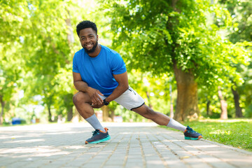 Smiling athlete stretching legs before outdoor workout. Young man in sportswear warming up in park on a sunny day.
