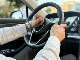A confident driver in a white shirt controls a business class car with one hand. A businessman's trip in sunny weather. The hand of a man holding the steering wheel of a car.