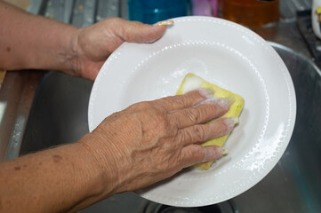 Elderly woman washing dishes in kitchen sink, only hands visible