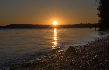 Sunrise on the lake shore. The sun rises from behind the hills. 