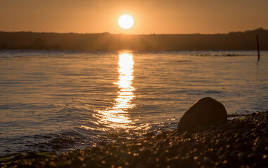 The sun rises from behind the hills. Sunrise on the lake shore.