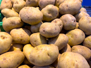 A close-up view shows a large pile of freshly harvested, unwashed potatoes with visible dirt and imperfections, highlighted by natural light.
