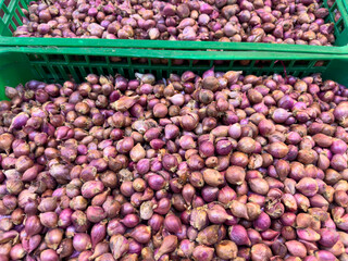 A large, full-frame, close-up view shows a vast pile of small, unpeeled red shallots with their thin papery skin, showcasing a rich purple and brown color.