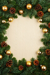 Christmas frame with gold baubles, green fir branches, and pine cones on a soft cream textured background. Festive background for greeting cards, invitations, packaging, or seasonal projects.