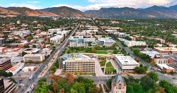 Lovely panorama of Salt Lake City with lush greenery. Drone footage over the lively city approaching the stunning mountains at backdrop.