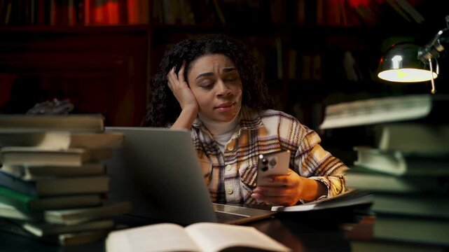 African American woman scrolling phone instead of studying, procrastination