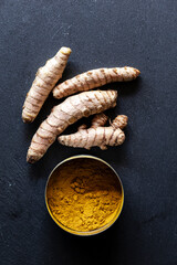 Fresh Turmeric Roots and Ground Powder on Dark Slate Background