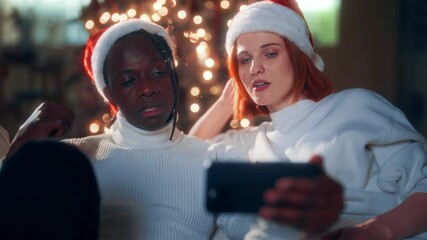 Portrait of man and woman chatting by video call in smartphone in Christmas. Modern technology of communication, biracial loving couple celebrating Xmas, smiling faces of black guy and caucasian lady