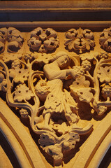 Stone relief in the cloister of Mont Saint Michel Abbey showing a monk harvesting grapes, symbol of monastic life, with warm light highlighting Gothic details and craftsmanship
