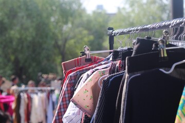 Roupas usadas penduradas em cabides em feira de moda circular
Second-hand clothes hanging on hangers at circular fashion flea market