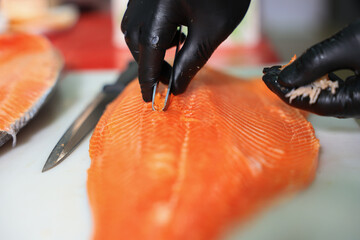 The chef is preparing, handling, deboning or slicing fresh salmon. Close up hand of chef with salmon sashimi.