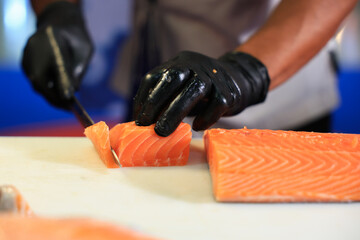 The chef is preparing, handling, deboning or slicing fresh salmon. Close up hand of chef with salmon sashimi.