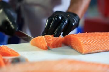The chef is preparing, handling, deboning or slicing fresh salmon. Close up hand of chef with salmon sashimi.