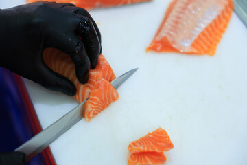 The chef is preparing, handling, deboning or slicing fresh salmon. Close up hand of chef with salmon sashimi.